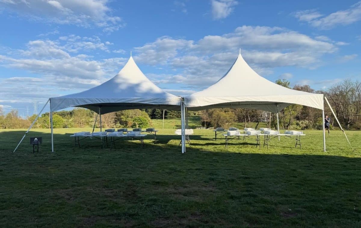 A 20 by 40 twin peak tent standing in an open field under a blue sky with rows of tables and chairs beneath it.