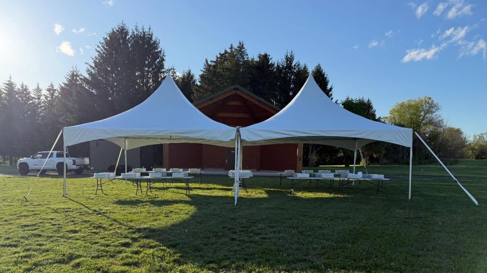 A twin peak tent on an open lawn in low evening sun, tables and chairs laid out underneath.
